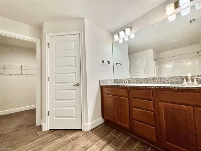 Bathroom featuring wood tiled floor, a sink, double vanity, and visible vents and view of walking closet