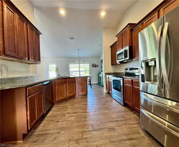 Kitchen featuring wood finish tile  floors, stainless steel appliances, an inviting chandelier, and a peninsula