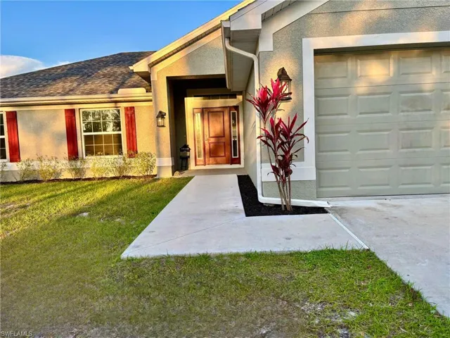 Doorway to property featuring a garage, stucco siding, and a lawn