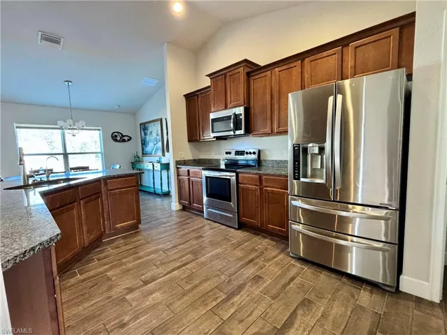 Kitchen with an inviting chandelier, stainless steel appliances, dark wood look tiles flooring, a sink, and visible vents