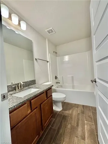 2nd Bathroom with a textured ceiling, tub / shower combination, visible vents, wood-finish tile floors, and vanity
