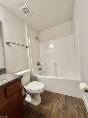 second Bathroom featuring vanity, toilet, shower/washtub combination, visible vents, and wood finish tile floors