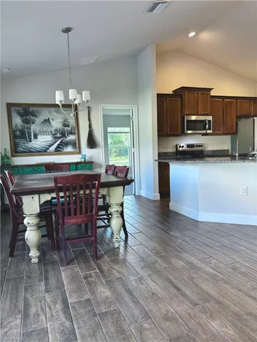 Dining room with vaulted ceiling, baseboards, visible vents, dark wood-type flooring, and an inviting chandelier