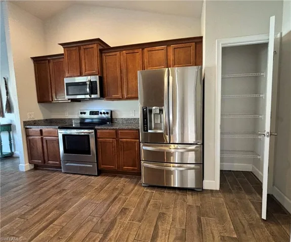 Kitchen with appliances with stainless steel finishes, lofted ceiling, baseboards, dark countertops, and dark wood-tile flooring and pantry