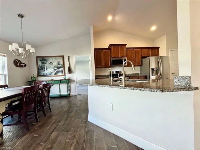 Kitchen featuring  wood-style tiles flooring, dark stone counters, a notable chandelier, and appliances with stainless steel finishes