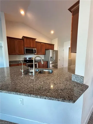 Kitchen with a granite peninsula, dark stone counters, stainless steel appliances, a sink, and vaulted ceiling