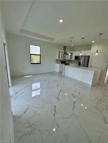 Unfurnished living room with light marble finish flooring, a raised ceiling, and recessed lighting