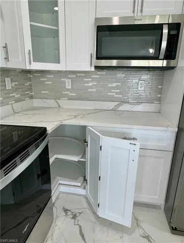 Kitchen with appliances with stainless steel finishes, white cabinetry, backsplash, light marble finish floors, and light stone countertops