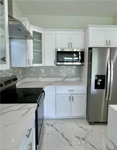 Kitchen with appliances with stainless steel finishes, light marble finish flooring, light stone counters, and backsplash