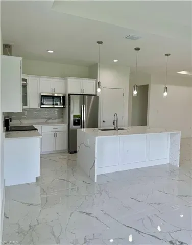 Kitchen featuring light stone countertops, backsplash, light marble finish floors, stainless steel appliances, and recessed lighting