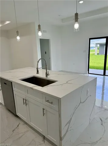 Kitchen with hanging light fixtures, light marble finish flooring, white cabinets, an island with sink, and light stone counters