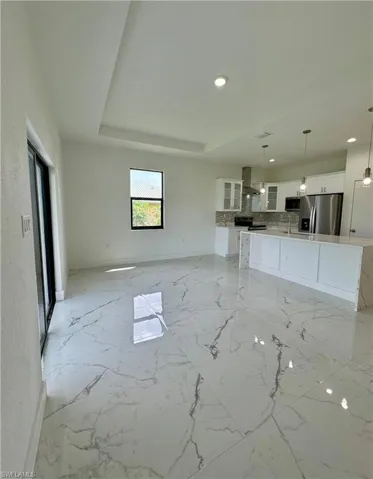 Unfurnished living room with light marble finish flooring, a tray ceiling, and recessed lighting
