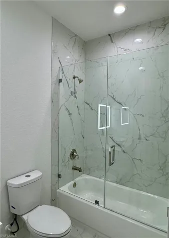 Bathroom featuring marble look tiles, enclosed tub / shower combo, and a textured wall