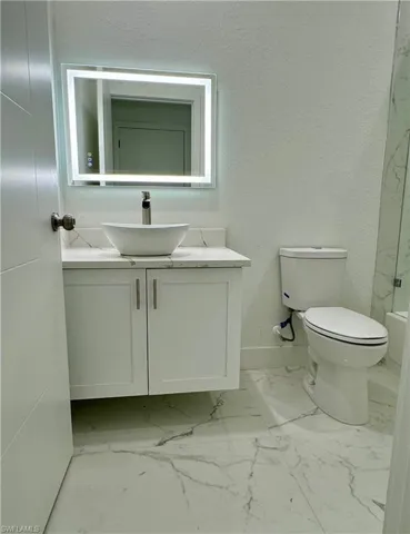 Full bath featuring vanity, a textured wall, and light marble finish flooring