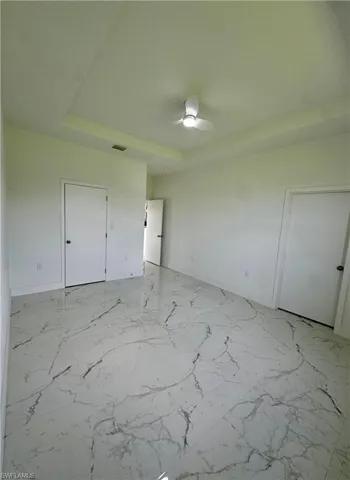 Unfurnished bedroom with a tray ceiling, light marble finish flooring, and ceiling fan