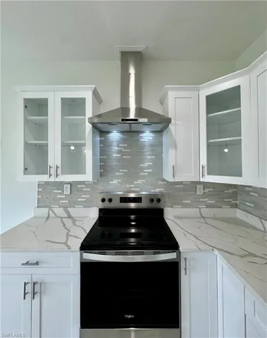 Kitchen featuring electric range, glass insert cabinets, light stone counters, and white cabinetry