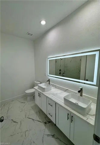 Bathroom with a marble finish shower, double vanity, a textured ceiling, light marble finish floors, and a textured wall