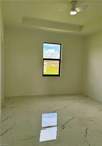 Spare room with a tray ceiling, light marble finish flooring, and a ceiling fan
