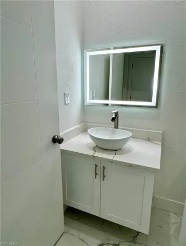 Bathroom featuring a textured wall, vanity, and light marble finish floors