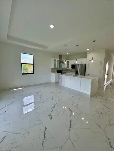 Unfurnished living room featuring light marble finish flooring, a raised ceiling, and recessed lighting