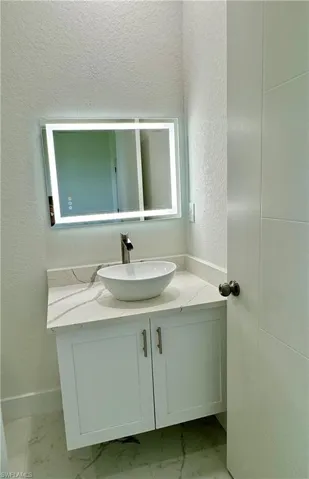 Bathroom with a textured wall, vanity, and light marble finish floors