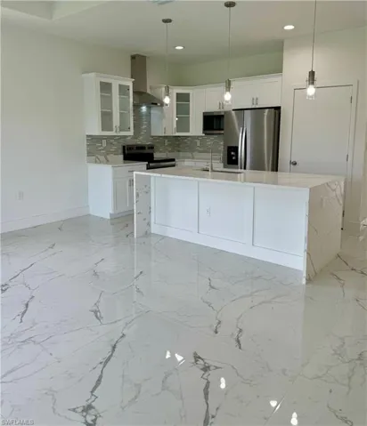 Kitchen featuring tasteful backsplash, glass insert cabinets, stainless steel appliances, light stone countertops, and white cabinetry