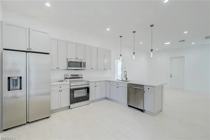 Kitchen with stainless steel appliances, hanging light fixtures, white cabinetry, and a peninsula