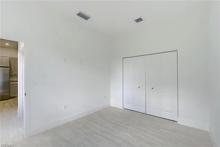 Unfurnished bedroom featuring stainless steel fridge, wood tiled floors, and a closet