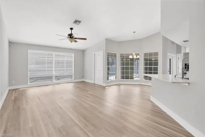 Unfurnished living room with a chandelier, light wood finished floors, vaulted ceiling, and ceiling fan