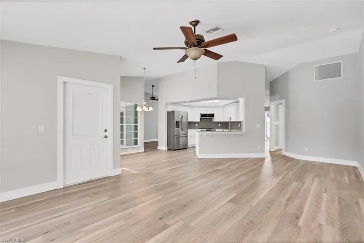 Unfurnished living room featuring vaulted ceiling, a chandelier, ceiling fan, and light wood-style flooring