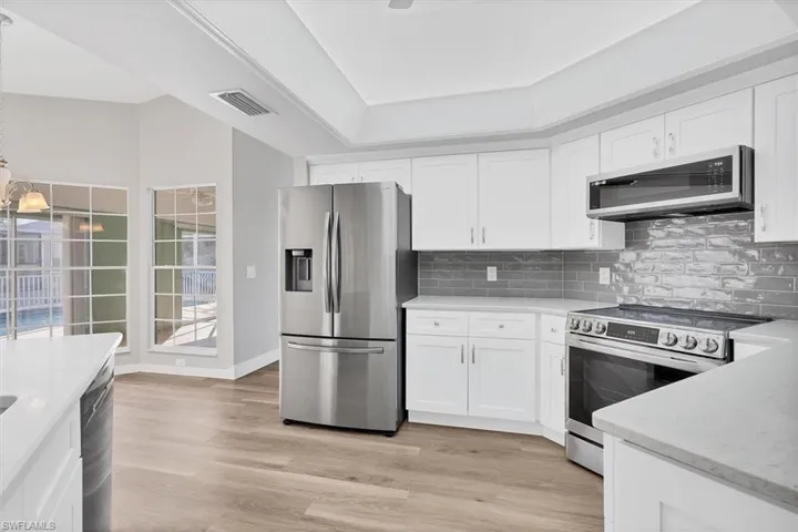 Kitchen featuring appliances with stainless steel finishes, white cabinetry, light stone counters, and light wood-style floors