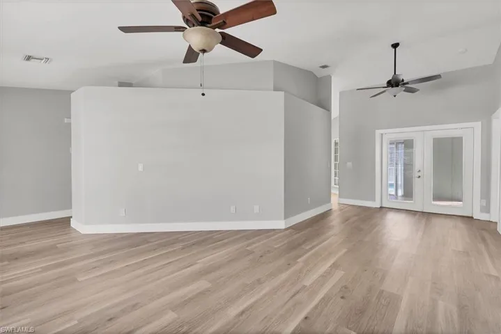 Unfurnished living room with french doors, light wood-style floors, ceiling fan, and high vaulted ceiling