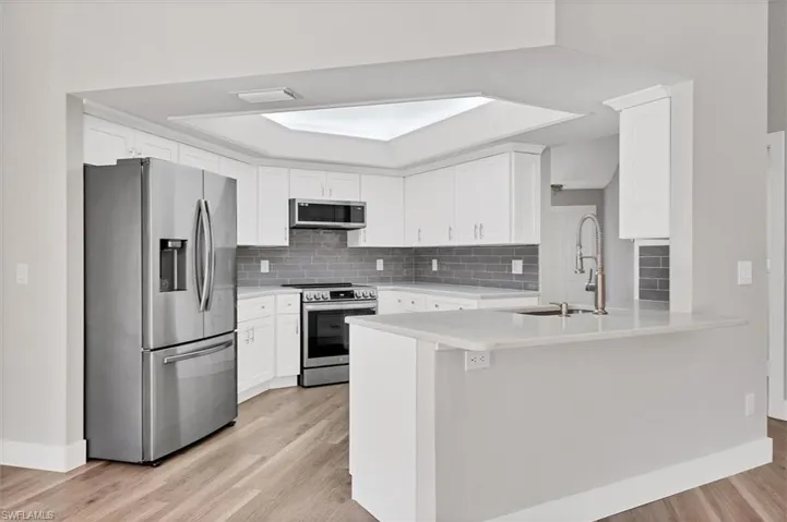 Kitchen featuring appliances with stainless steel finishes, white cabinets, a peninsula, and tasteful backsplash