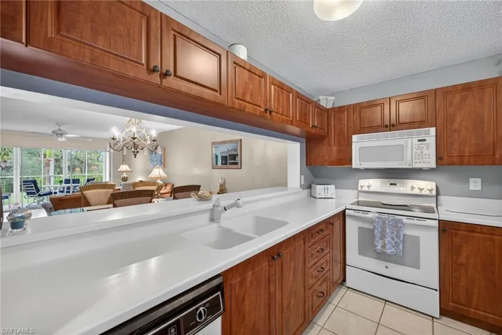 Kitchen featuring white appliances, a chandelier, light countertops, brown cabinets, and light tile patterned flooring
