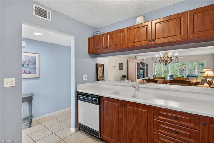 Kitchen with light countertops, a chandelier, brown cabinetry, dishwasher, and a textured ceiling