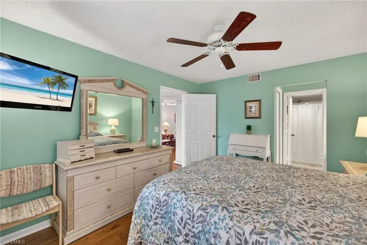 Bedroom featuring dark wood-style floors, a ceiling fan, a textured ceiling, and ensuite bath