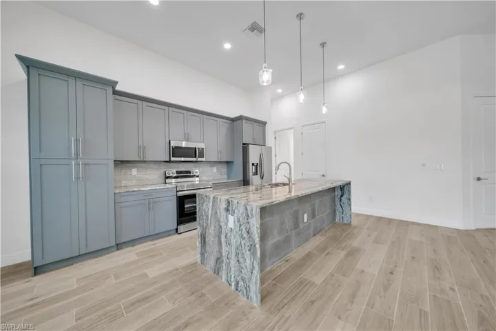 Kitchen with wood finish floors, stainless steel appliances, hanging light fixtures, and light stone counters