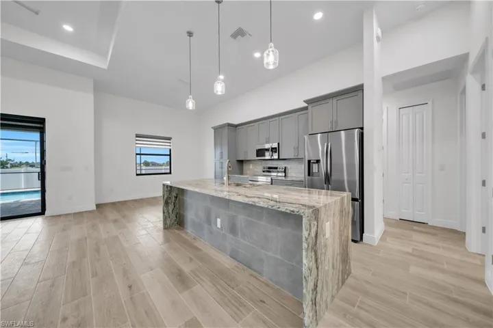 Kitchen featuring gray cabinetry, decorative light fixtures, stainless steel appliances, wood tiled floors, and light stone countertops