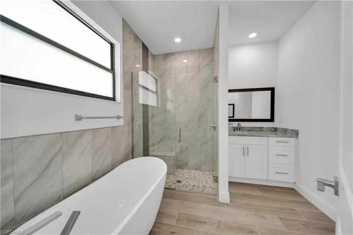 Bathroom with a marble finish shower, vanity, a soaking tub, wood tiled floors, and recessed lighting