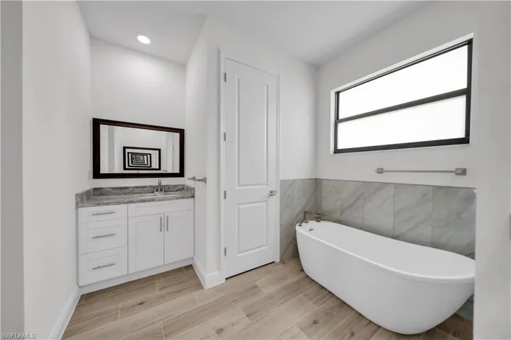 Bathroom with vanity, wood finish floors, a freestanding tub, tile walls, and recessed lighting