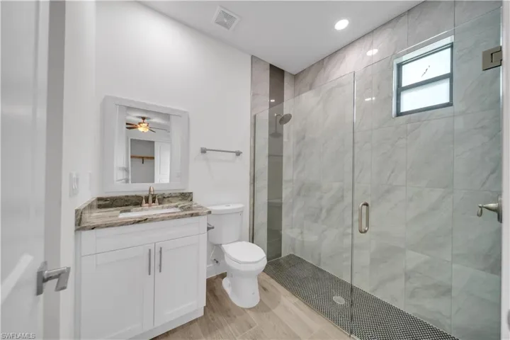 Bathroom featuring vanity, a stall shower, wood finish floors, and recessed lighting