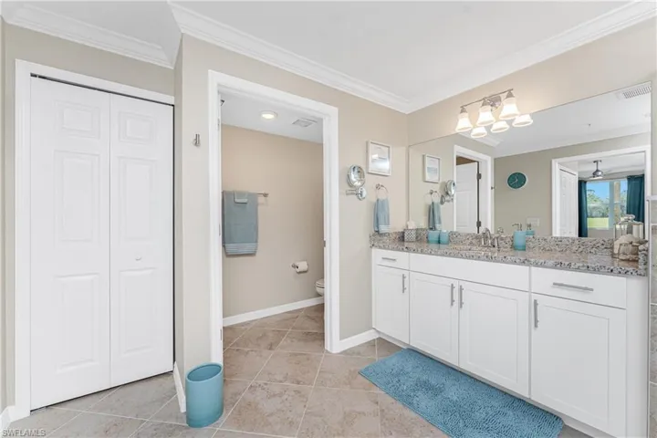 Bathroom with a closet, ornamental molding, vanity, and light tile patterned floors