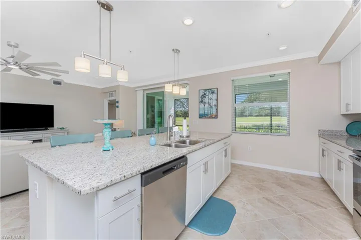 Kitchen with white cabinets, decorative light fixtures, appliances with stainless steel finishes, light stone countertops, and crown molding
