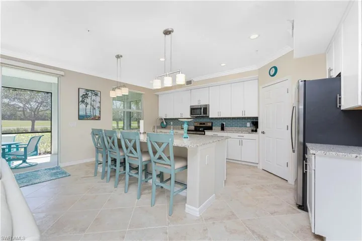 Kitchen with ornamental molding, decorative backsplash, decorative light fixtures, white cabinetry, and a breakfast bar