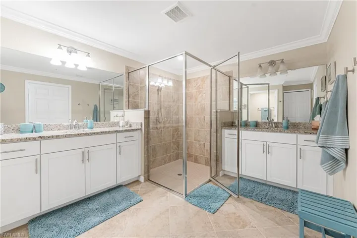 Bathroom featuring ornamental molding, light tile patterned floors, a shower stall, and two vanities