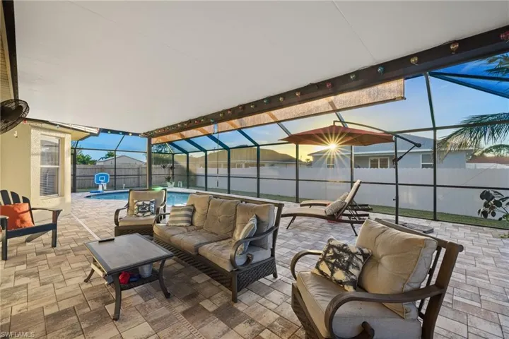 Large, screened pool enclosure with outdoor living space, roll down shades, & pavered tiles