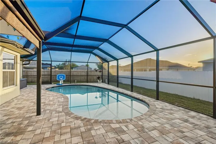 Large, screened pool enclosure with outdoor living space, roll down shades, & pavered tiles