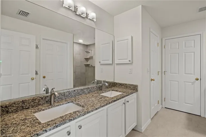 En Suite Bath with granite counter top dual vanity, walk-in shower, walk-in closet, and extra closet