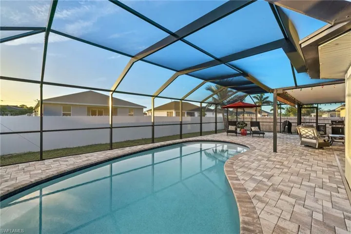 Large, screened pool enclosure with outdoor living space, roll down shades, & pavered tiles