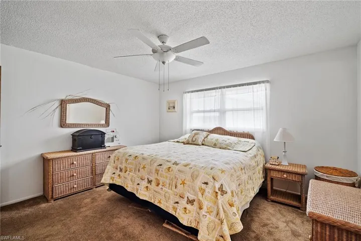 Bedroom featuring ceiling fan, dark colored carpet, and a textured ceiling